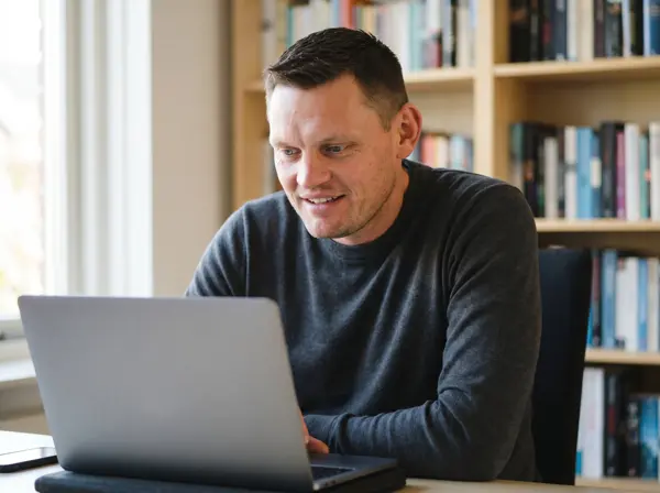 Remco zit aan bureau met laptop, kantoor met boekenkasten op achtergrond, webdesign voor coaches